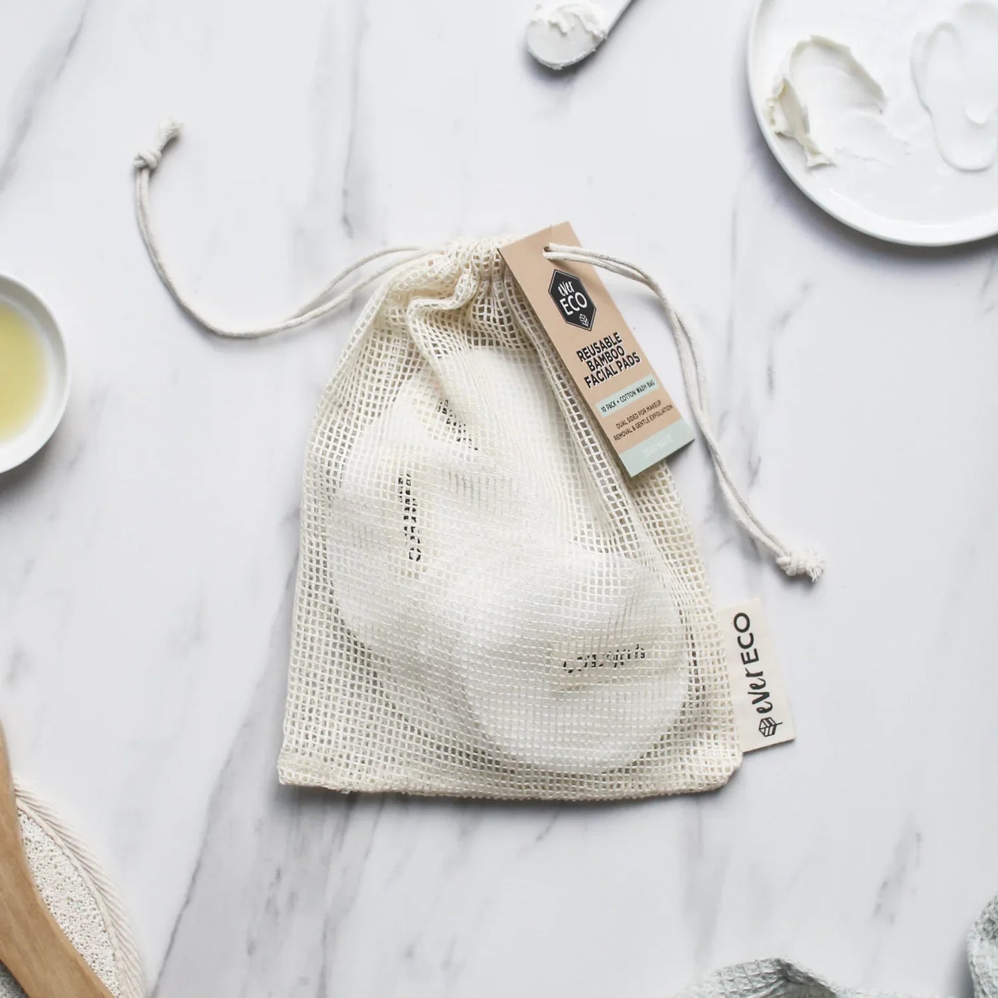 Eco-friendly reusable bamboo facial pads with cotton wash bag on a marble surface.