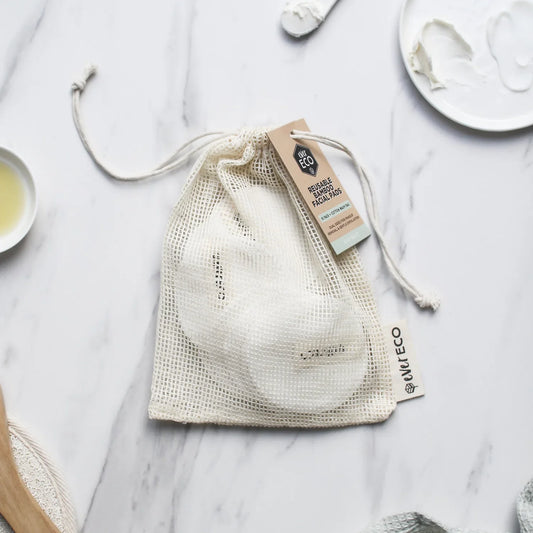 Eco-friendly reusable bamboo facial pads with cotton wash bag on a marble surface.