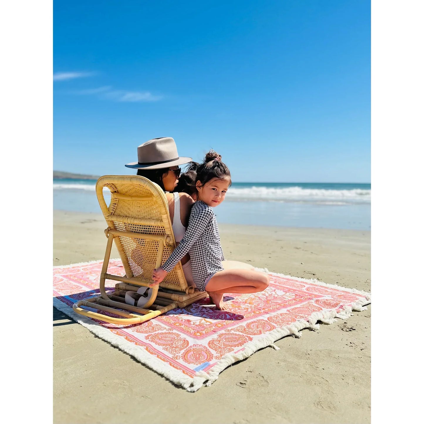 Picnic Mantra Eloise Picnic Rug/Woven Throw on a beach with a child and adult sitting on it, featuring bohemian floral design and tassel edging.