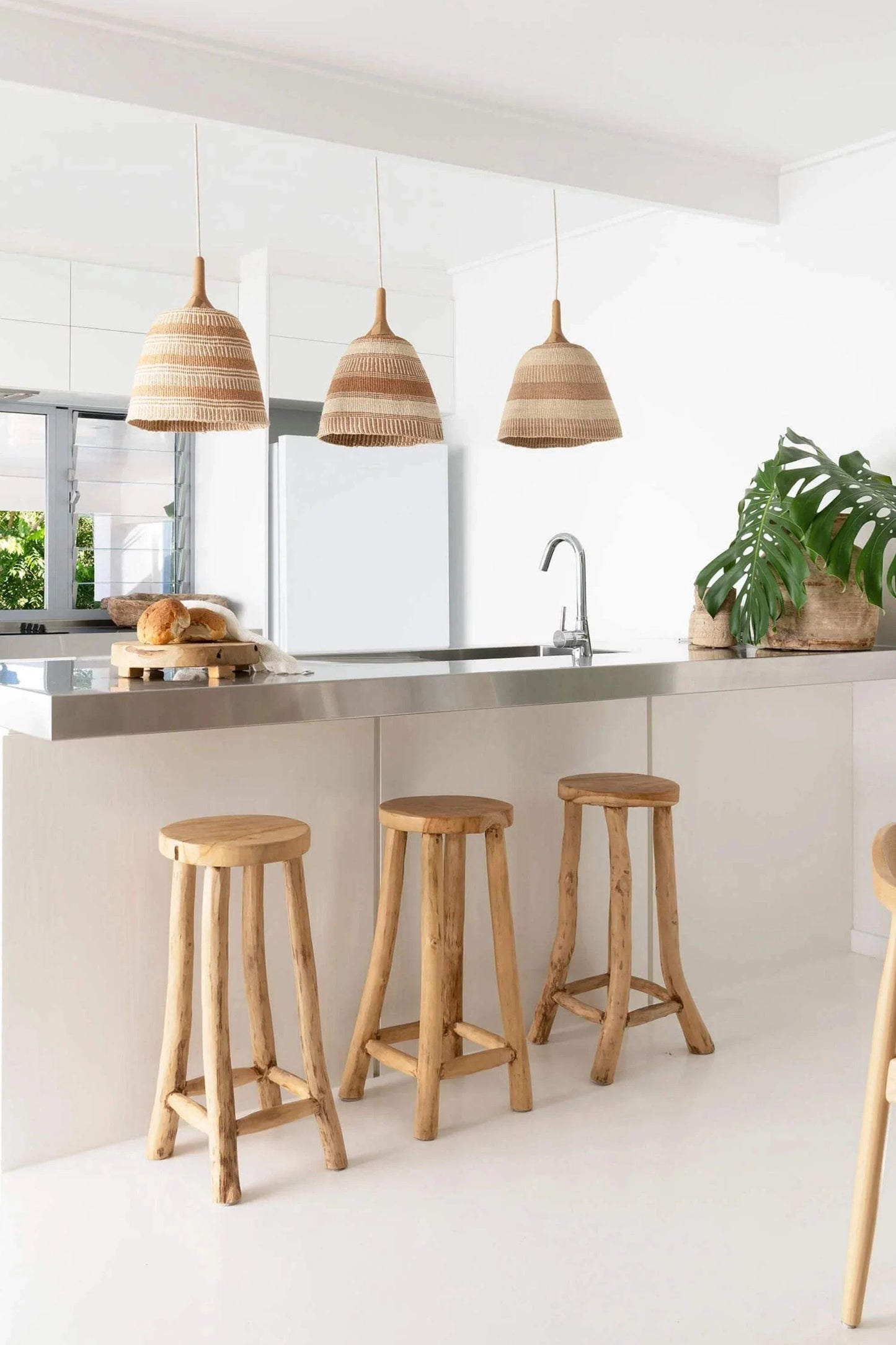 Bespoke woven pendant lights hanging over a kitchen island with wooden stools.