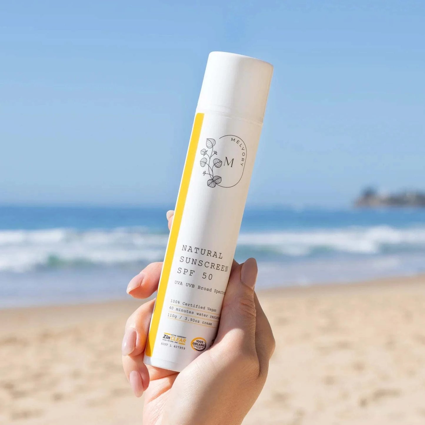 Melvory Natural Sunscreen SPF 50+ held by a beach with ocean backdrop