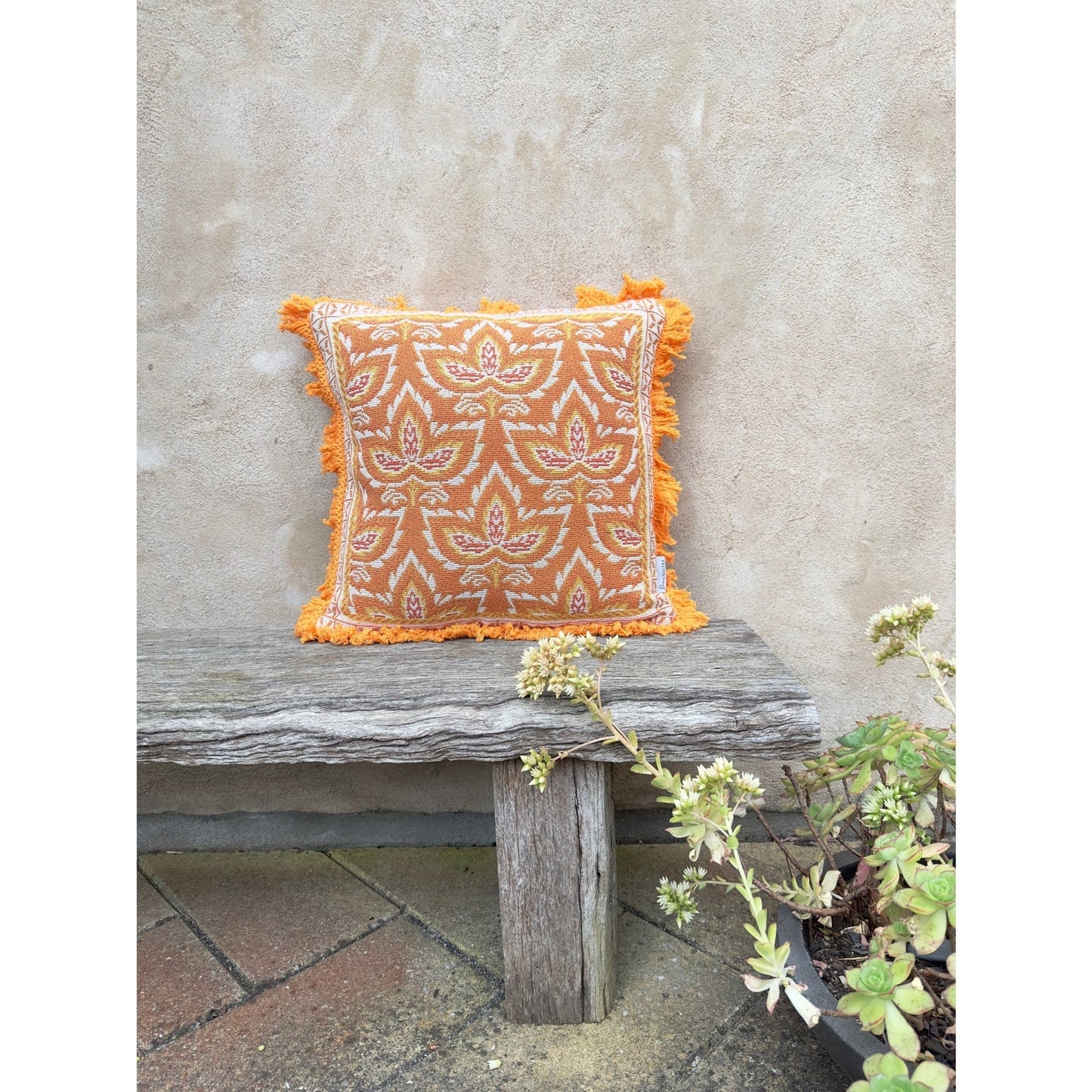 Orange floral Kaia scatter cushion on wooden bench, inspired by autumn flora; eco-friendly with recycled PET fiber filling.