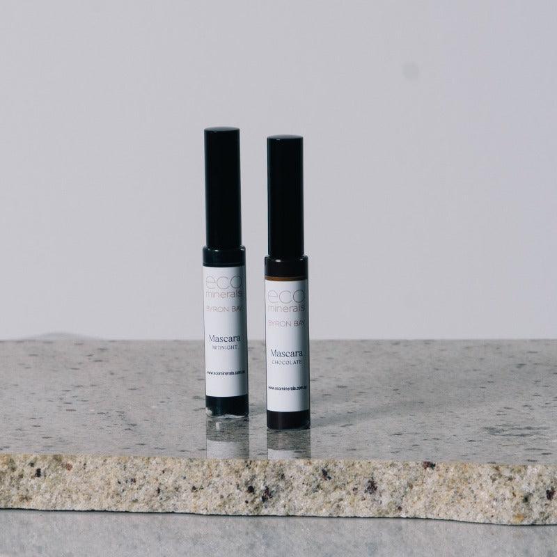 Eco Minerals Mineral Mascara tubes in Midnight Black and Chocolate Brown on a marble surface.