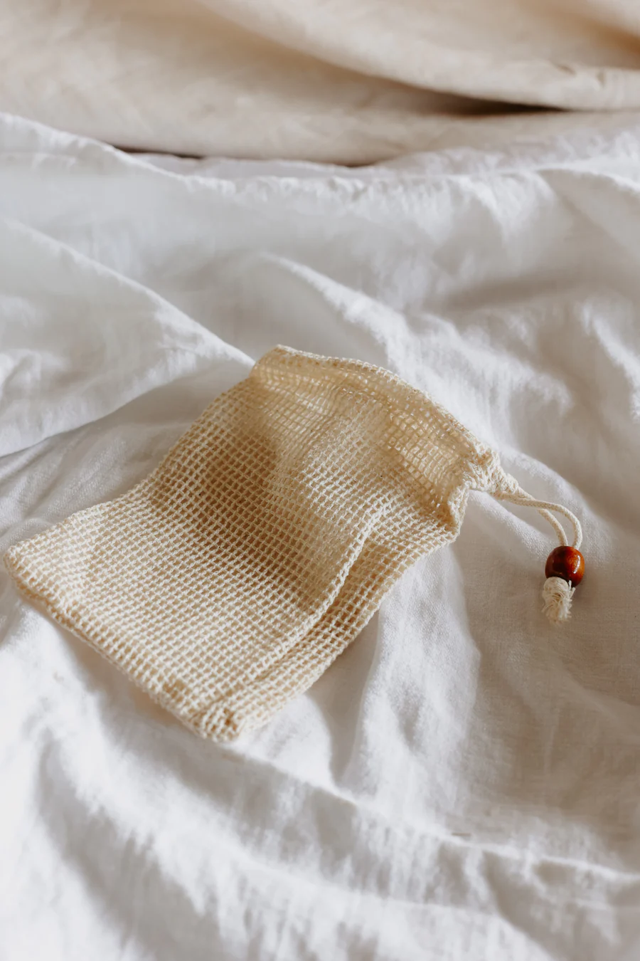 Apiary Made soap bag made from 100% organic undyed cotton laying on a fabric surface.