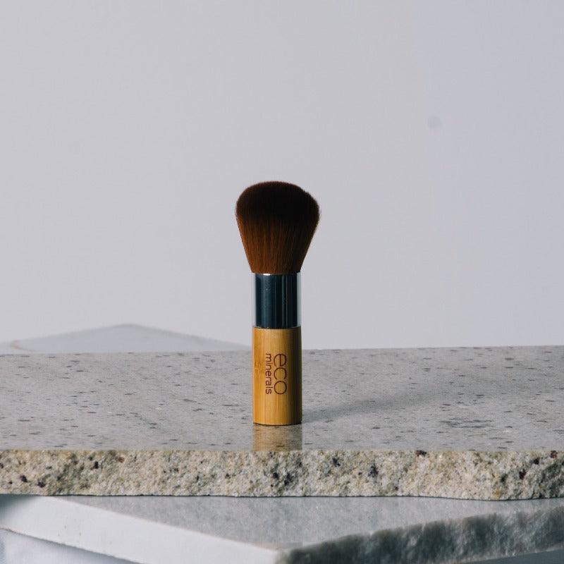 Eco Minerals Vegan Kabuki Brush on a stone surface.