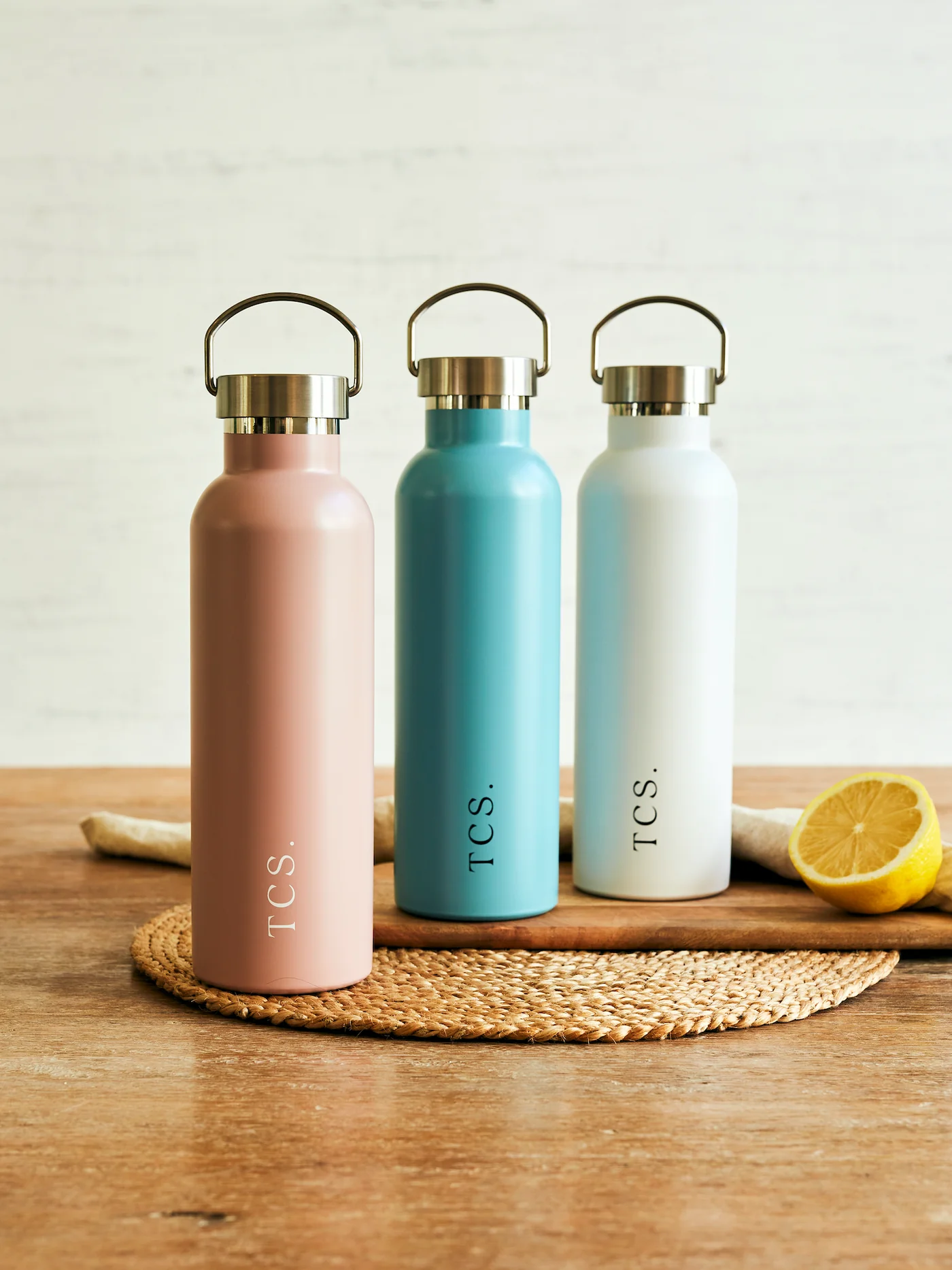 Insulated stainless steel water bottles from The Conscious Store in pastel colors on a wooden surface.
