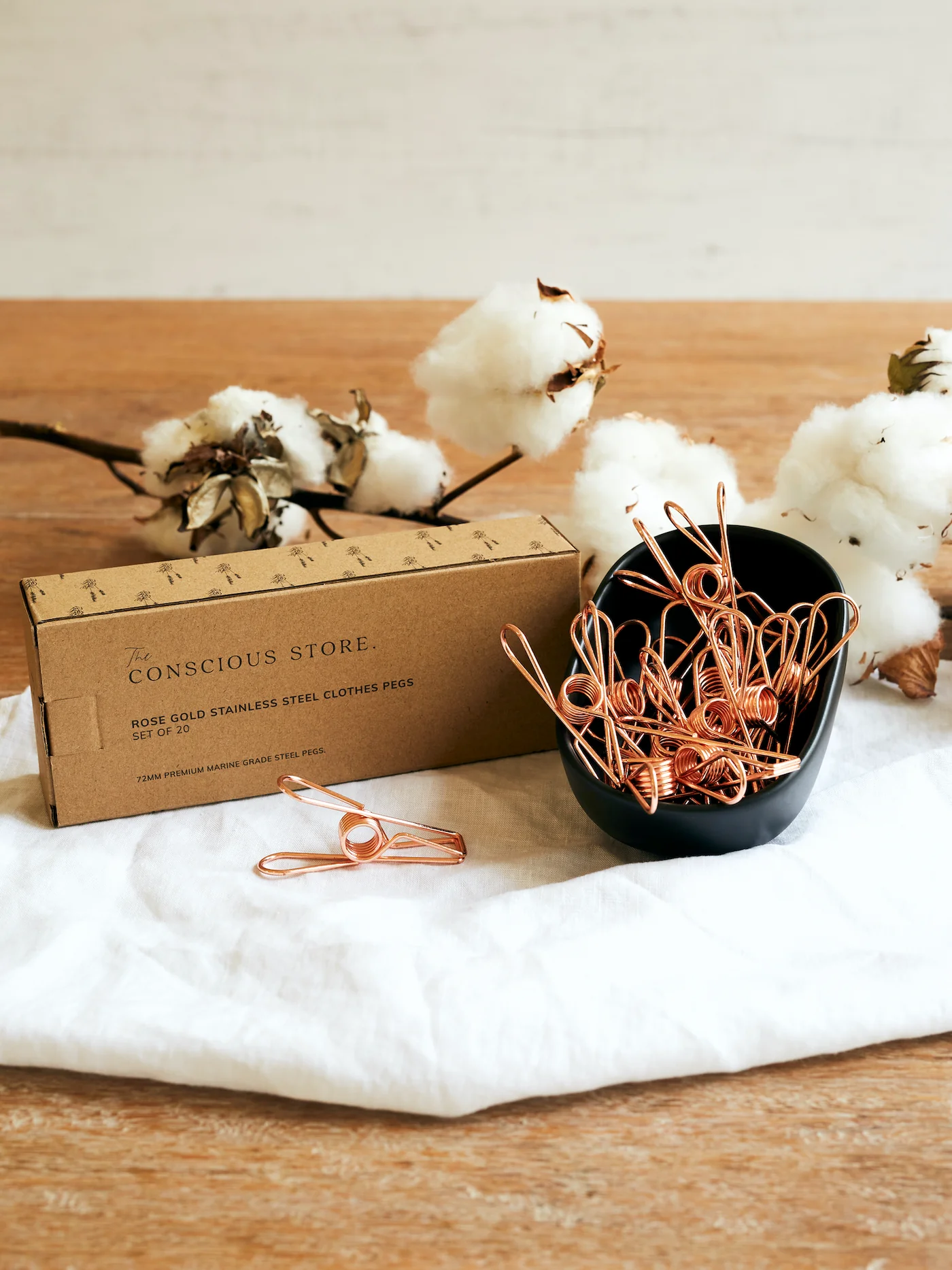 Rose gold stainless steel pegs set with box on fabric surface.