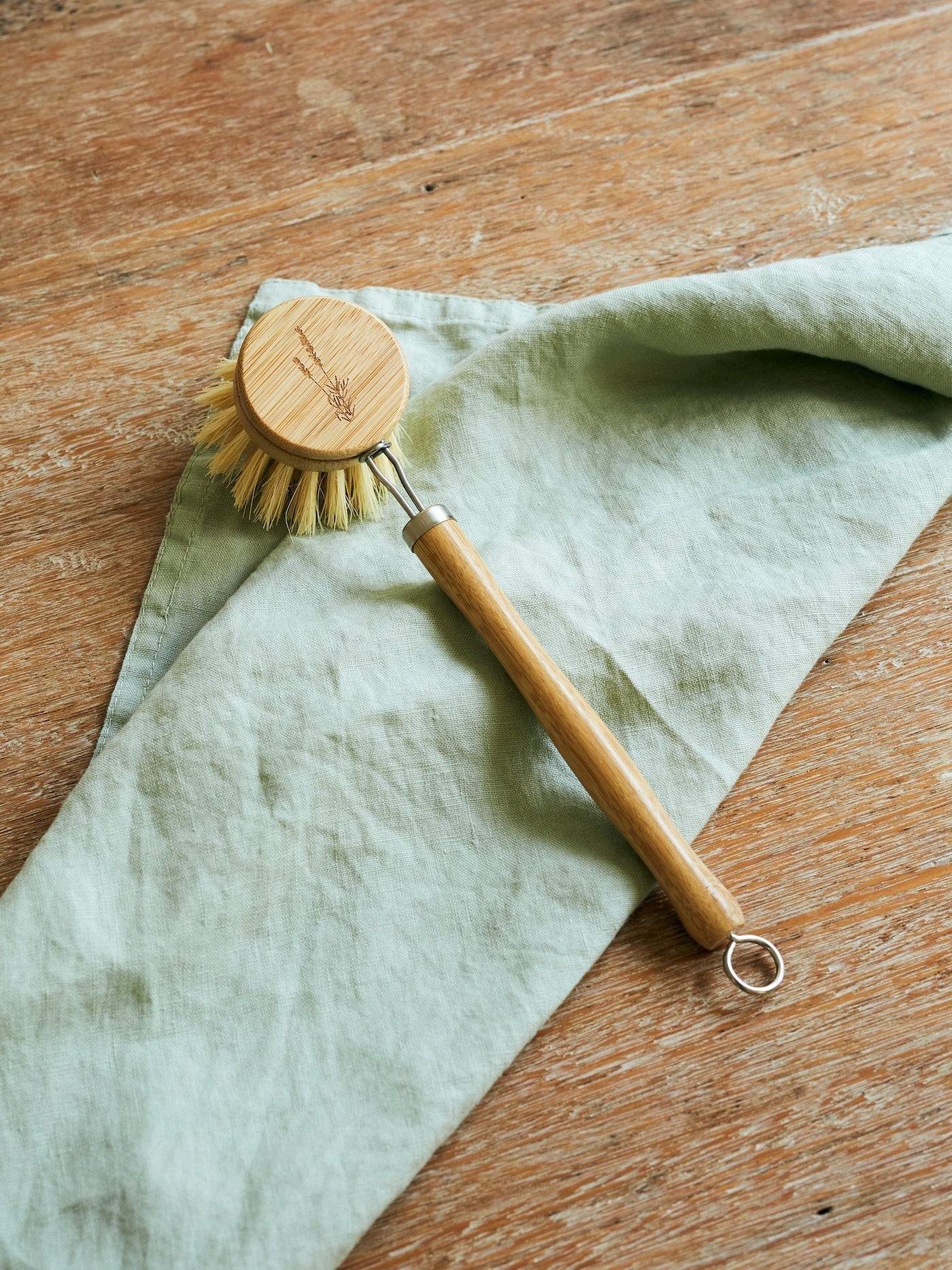 Bamboo dish brush with sisal bristles on wooden surface and green cloth.