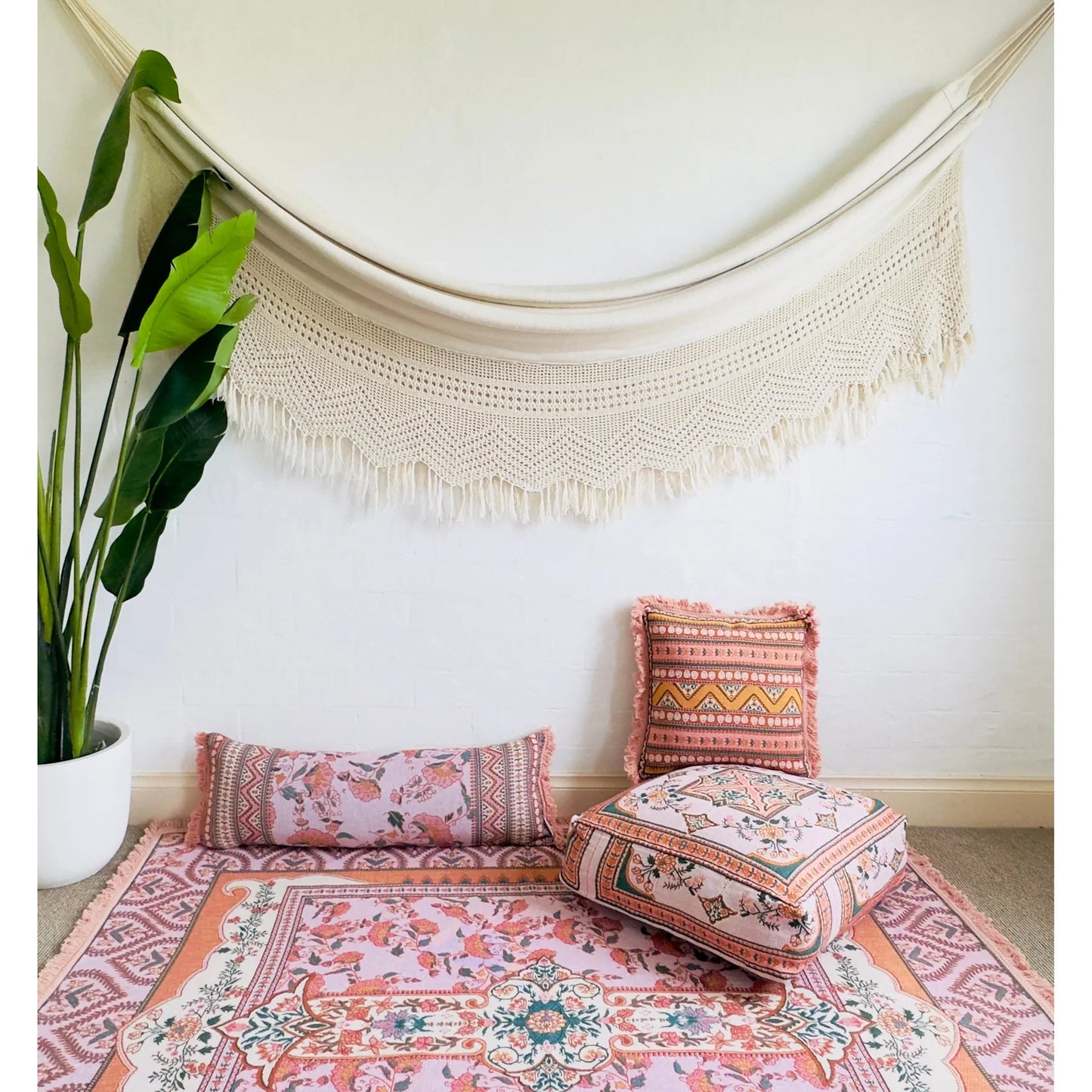 Avalene picnic rug with floral design and tassels, Victorian-inspired, pink and coral palette, on wooden floor with cushions.
