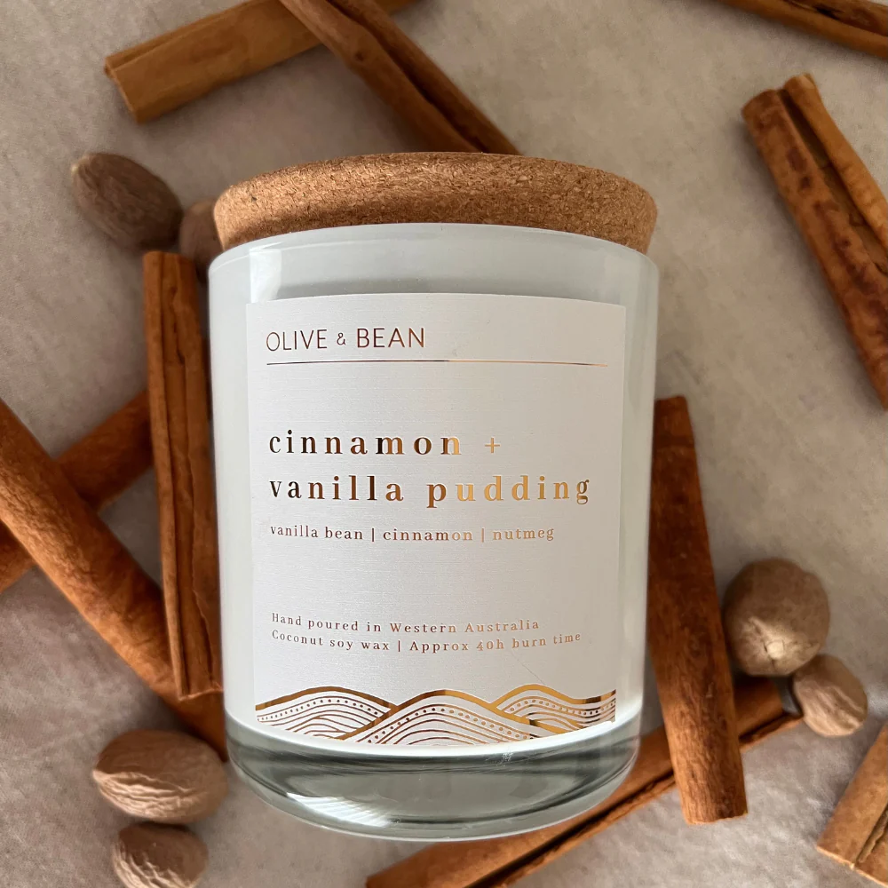 Olive & Bean cinnamon and vanilla pudding scented candle with natural coconut soy wax and wood wick surrounded by cinnamon sticks and nutmeg.