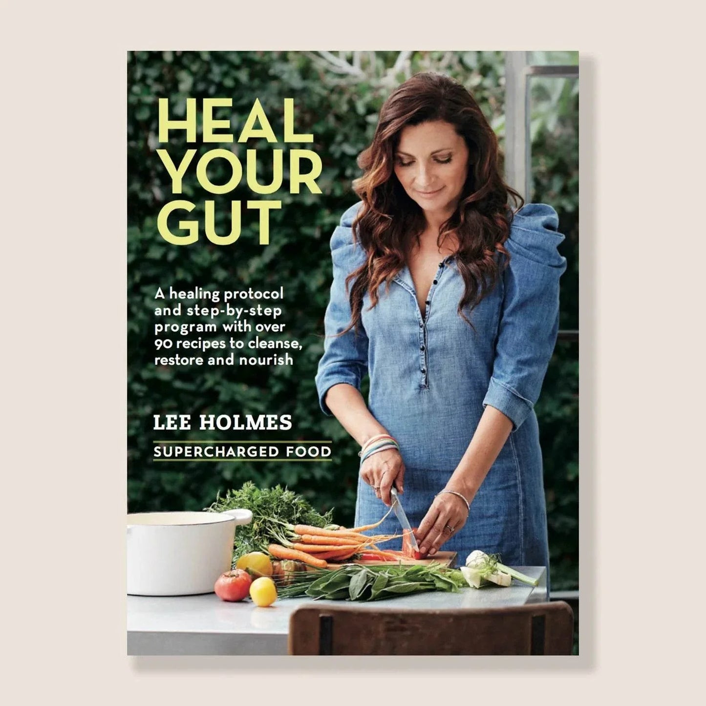 Book cover of "Heal Your Gut" by Lee Holmes, featuring a woman preparing fresh vegetables.