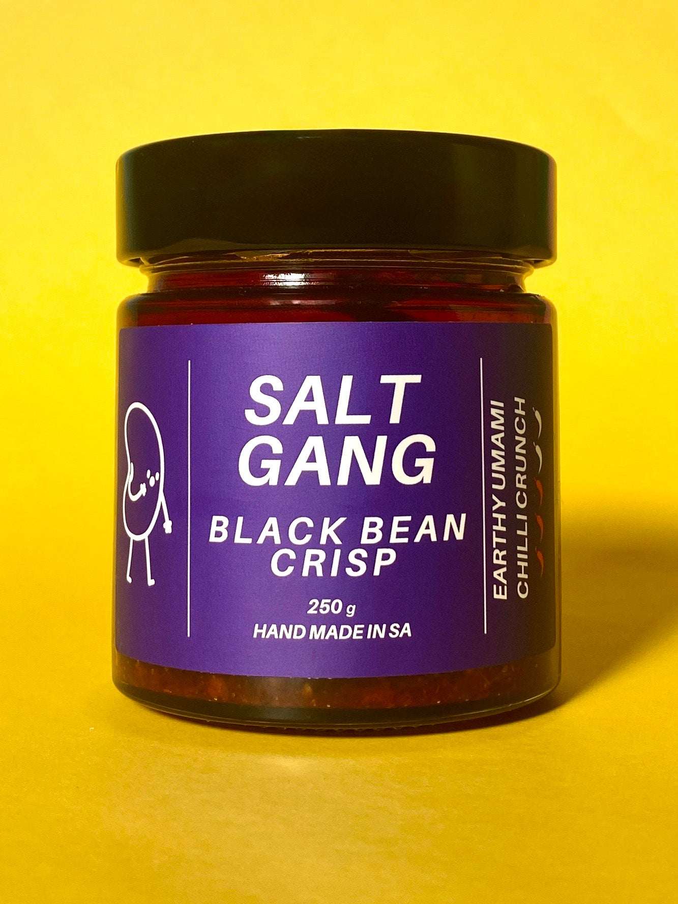 Salt Gang Black Bean Chilli Crisp in glass jar with purple label on yellow background.