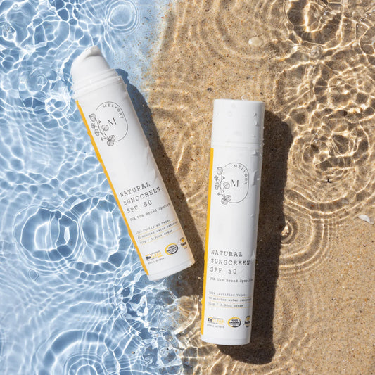 Melvory Natural Sunscreen SPF 50+ bottles on sandy beach with ocean waves.